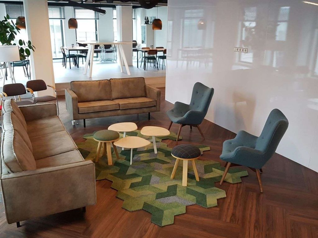 Loungehoek met een 3- en een 2 zitsbank, losse tafeltjes en 2 klassieke oorfauteuils. Kleed gemaakt van hergebruikte tapijttegels in geometrische vormen gesneden